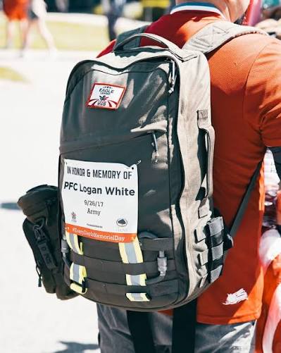 A participant carrying a ruck bearing a memorial sign for PFC Logan White, Army